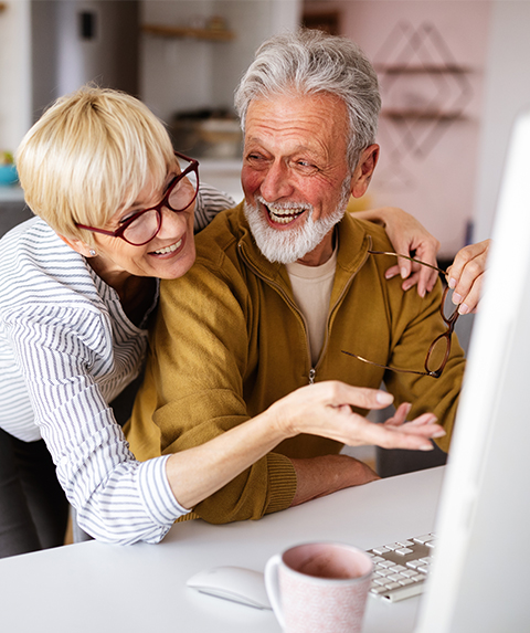 happy senior couple laughing in front of computer wealth management