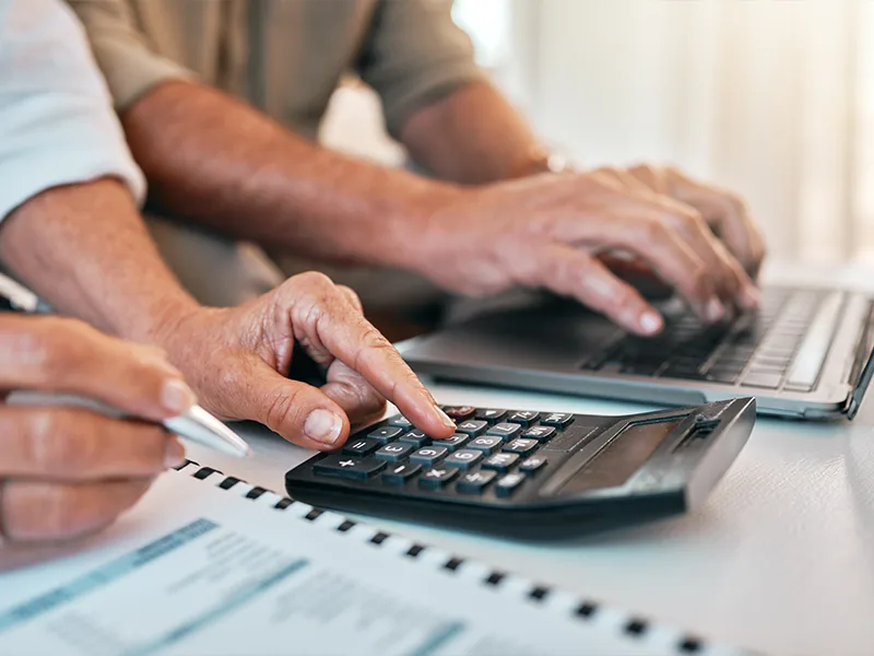 close up of hands using calculator and laptop researching insurance products